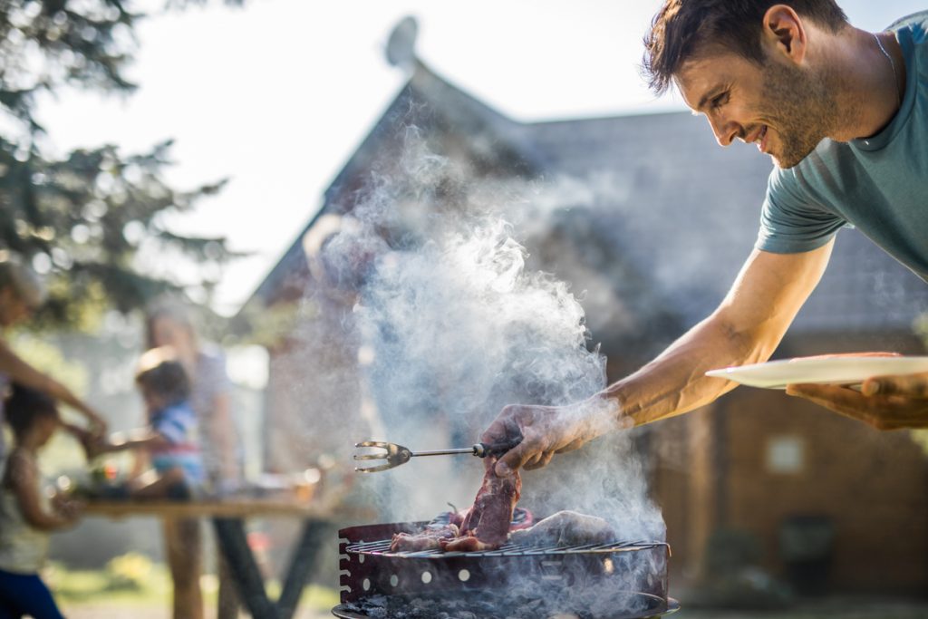 Happy man grilling meat on a barbecue grill outdoors.