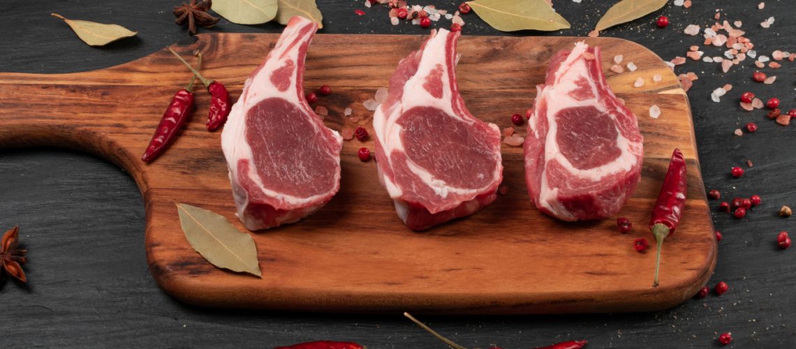 Raw lamb chops or mutton cuts with salt and spices on black stone background. Fresh sheep ribs cutlet with bone on wood cutting board closeup